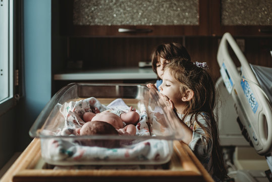 Siblings looking at newborn brother in hospital bassinet