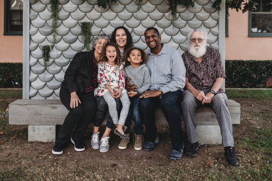 Portrait Of Multigenerational Family Sitting On Park Bench Outside