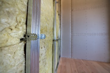 Wall of a room under renovation with mineral rock wool insulation and metal frame prepared for drywall plates.