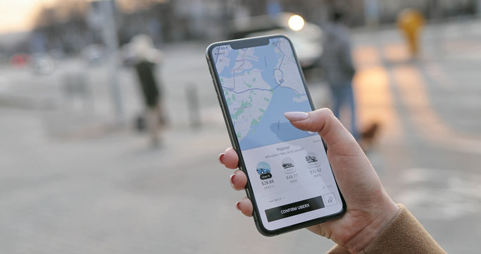 New York - Mar 20, 2020: Close Up Of Smartphone In Female Caucasian Hands. Woman Using Phone And Ordering Car At Uber Application. Girl Calling In And Booking Taxi At UberX App Outdoors.