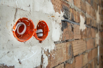 Socket orange boxes with wires in a wall. Cabling installation of electrical wires sticking out from electrical sockets hole on brick wall.