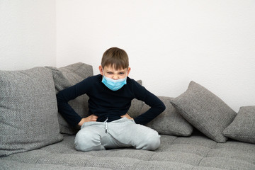 Offended angry boy sits in a mask at home in quarantine. Epidemic of coronavirus COVID19. Place for your message. Quarantined child at home isolated. Self isolation in home. Place for text