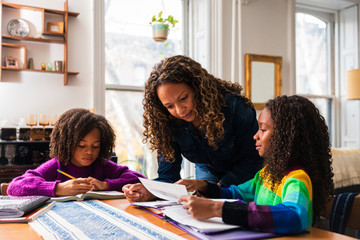Mother assisting daughters studying at table in living room