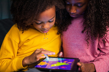 Sisters playing video game on digital tablet at home