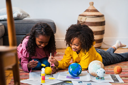 Sisters painting sphere while making solar system at home