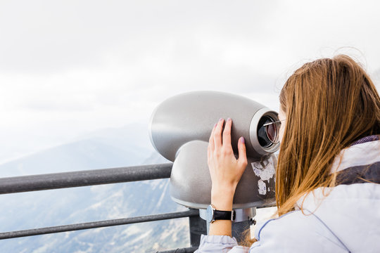 young women looks at mountain views in binoculars from observation