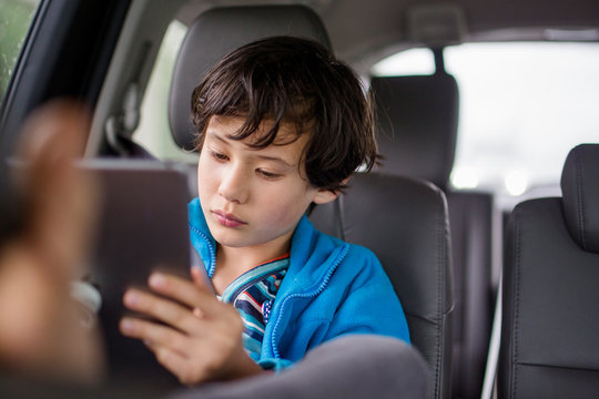 A Boy Sits In A Carseat On A Car Trip Watching A Tablet