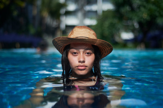 Stylish trendy young teen visco girl in the pool wearing a straw hat