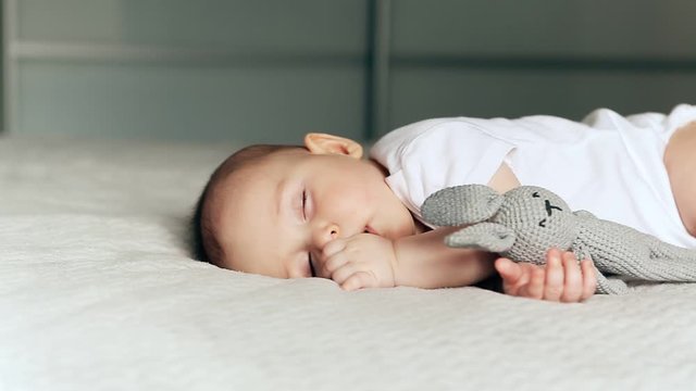 Sleeping cute baby boy on a blanket with a grey hare in hand