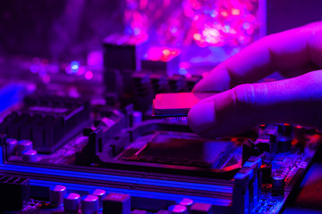 Motherboard in neon light. A hand inserts a processor into a socket on the motherboard. Computer service..