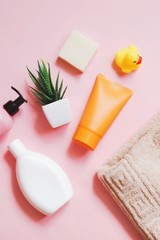 Obraz na płótnie Canvas liquid soap, white shampoo bottle, orange cream tube, aloe vera, yellow rubber duck and beige cotton towel on a pink background. Hair and skin care cosmetic products. Flat lay beauty photography