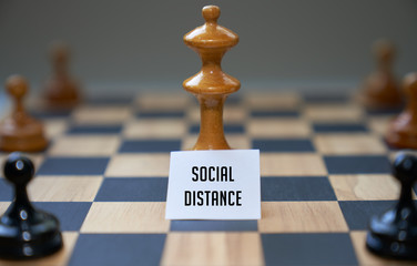 Concept chess pieces express social distancing with white board and text social distance in front of the center piece on the chess board.