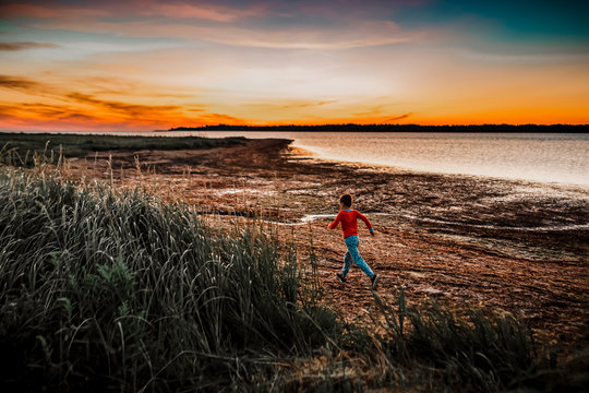 7 years old boy running at sunrise to find sea shells