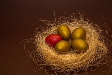 Easter golden eggs and one red egg in the decorative nest on dark background. Easter concept. Happy Easter greeting card.