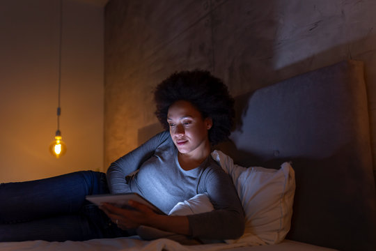 Woman lying in bed reading an e book on tablet computer