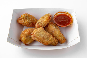 Chicken wings or drumsticks in a crispy batter with sauce in a paper plate for take away or food delivery isolated on a white background.