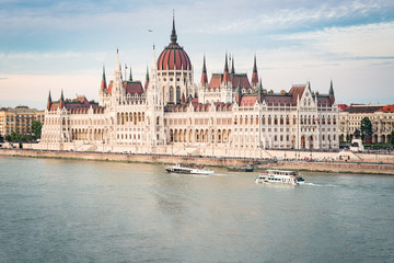 Fototapeta na wymiar The Budapest Parliament at sunset. Boats passing by on Danube river, Hungary 2019