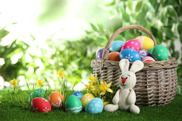 Colorful Easter eggs and toy rabbit on green grass. Space for text