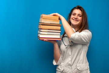 young beautiful funny girl the nurse holds many books on a blue background and is smiling, the student is studying in a medical college