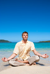 Fototapeta na wymiar Calm man sitting cross-legged in the waves meditating on the shore of a tropical beach