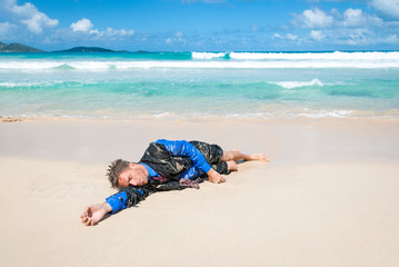 Castaway survivor businessman washed up on a tropical beach in a ragged torn suit
