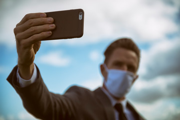Businessman wearing protective surgical face mask standing outdoors taking a smartphone selfie