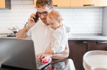 Handsome young man working at home with a laptop with a baby on his hands. Stay home concept. Home...