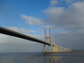 Obraz premium The Vasco de Gama Lisbon bridge crosses the river Tejo and reflects on the water illuminated by a ray of sunshine.