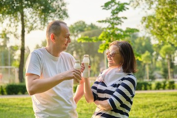 Obraz premium Happy mature couple in park, resting drinking yogurt, dairy after sports exercises