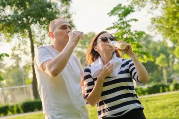Happy mature couple in park, resting drinking yogurt, dairy after sports exercises
