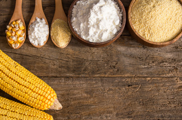 Corn flour and starch in wooden bowl and spoon with dried corn groats, kernels on rustic table. corn ingredients concept