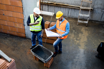 Men in hardhat and yellow and orange jacket posing on building site