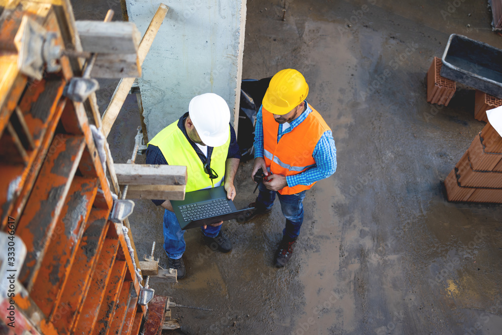 Wall mural men in hardhat and yellow and orange jacket posing on building site