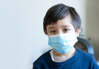 Kid in isolation wearing medical protection face mask with sad face,Child boy feeling bored have to stay at home during corona virus home quarantine, Protective measures against spreading of Covid-19