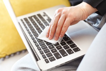 woman wiping laptop keyboard with disinfection wipes due to corona virus risk