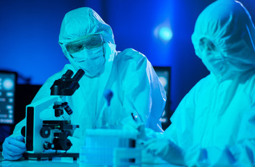 Scientists in protection suits and masks working in research lab using laboratory equipment:...