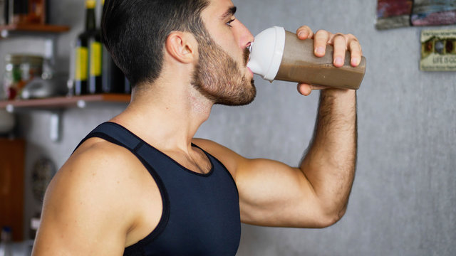 Young athletic man drinking a healthy smoothie drink or a protein shake from blender or shaker at home in kitchen - Powered by Adobe