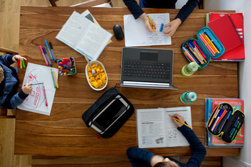 Three children, sitting around the table, writing school tasks while homeschooling