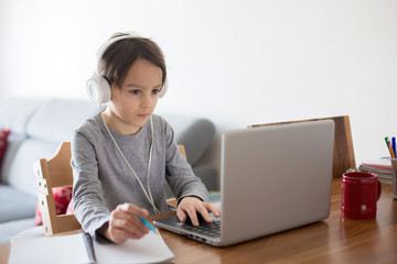 School child, sitting at the table with laptop, writing school tasks while homeschooling