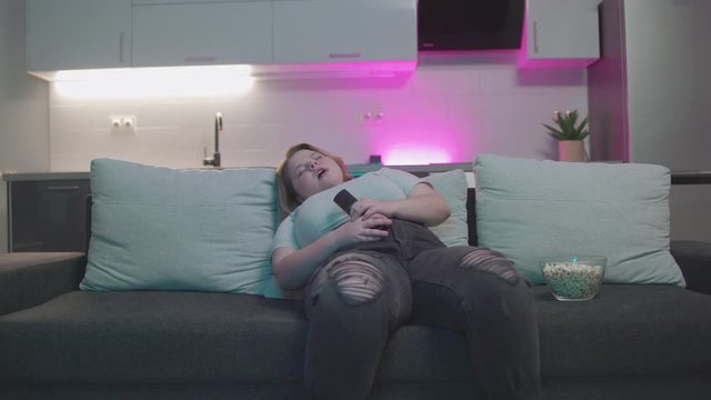 Young overweight woman falling asleep in front of tv, sedentary lifestyle