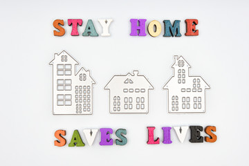 Words: Stay home, saves lives, made from wooden letters and three metalic houses, concept of self quarantine at home as preventative measure against corona virus Covid 19 outbreak.
