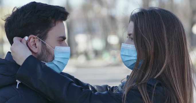 Young woman putting protective mask on her boyfriend's face