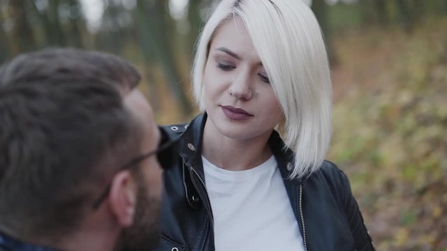 Pretty blonde in love talking with her brutal biker and smiling outdoors