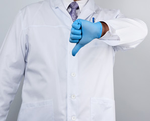 doctor in a white coat with buttons shows a gesture of dislike with his hand, wearing blue medical glove