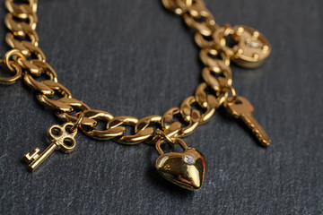 Golden bracelet with keys and a heart on a stone background.