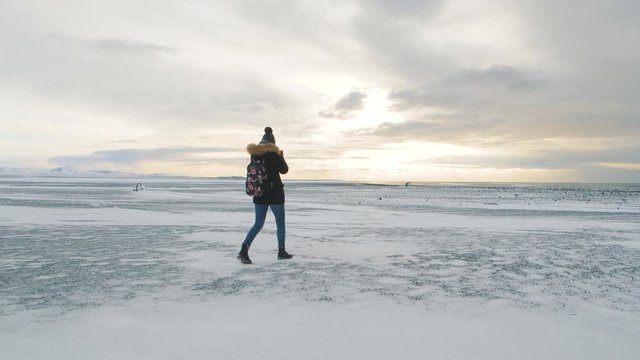 Young beautiful woman traveler with camera walking on snow desert in Iceland. Slow motion shot at sunset or sunrise. Around Solheimasandur dc3 Plane crash area 