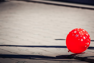 Lonely red balloon with a pattern of white stars lies on the sidewalk