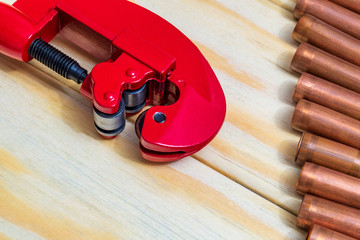 Red pipe cutter and copper pipes with connectors for plumbing repairs on wooden boards closeup