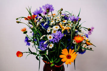 Bouquet of different spring wildflowers in a brown clay jug