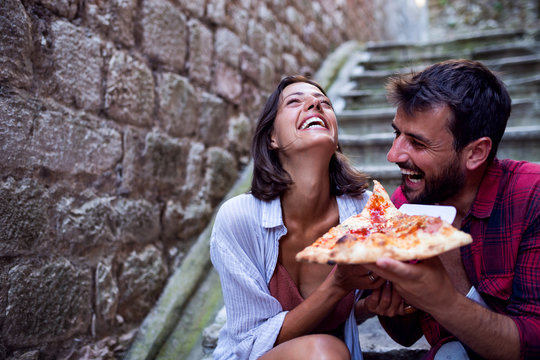Fototapeta Smiling love couple eating pizza at street